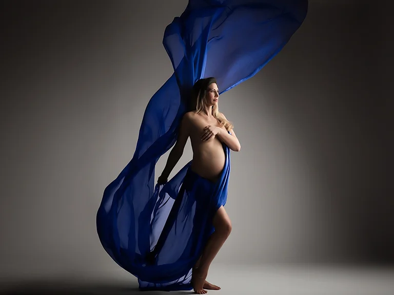 Femme enceinte drapée d’un voile bleu en mouvement, photo de grossesse en studio à Genève